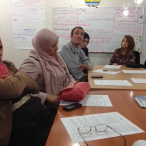 Training participants sit at table with charts behind them.